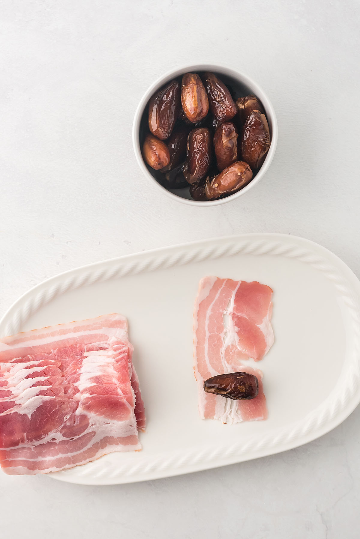 raw bacon halves and a bowl of dates on a counter