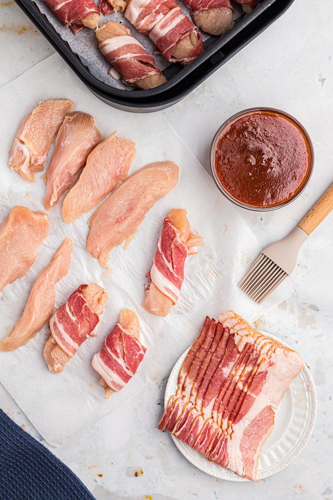 Chicken strips that are wrapped in raw bacon on a countertop