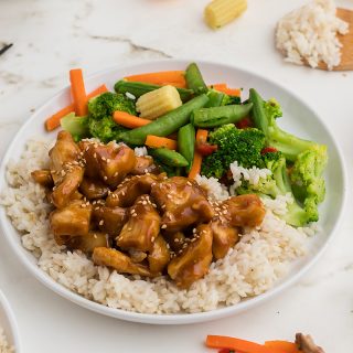 A close up of a plate of orange chicken with vegetables