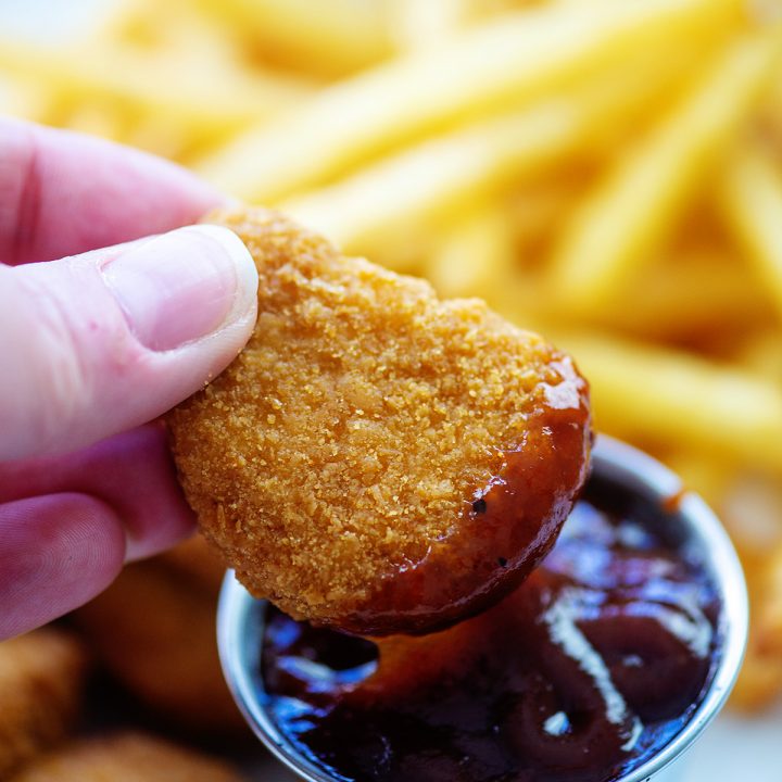 A close up of a woman dipping a chicken nugget in a bbq sauce