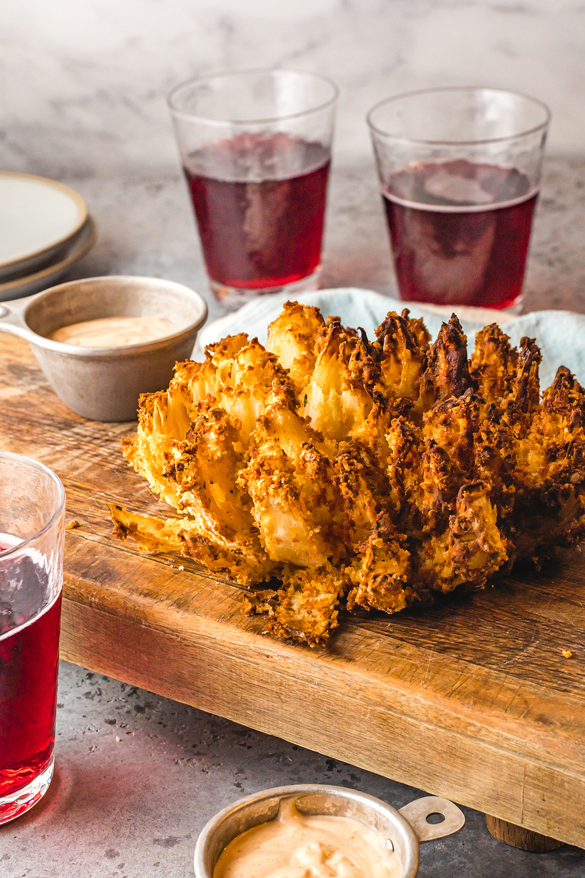 Blooming onion on a serving tray next to a cup of dipping sauce