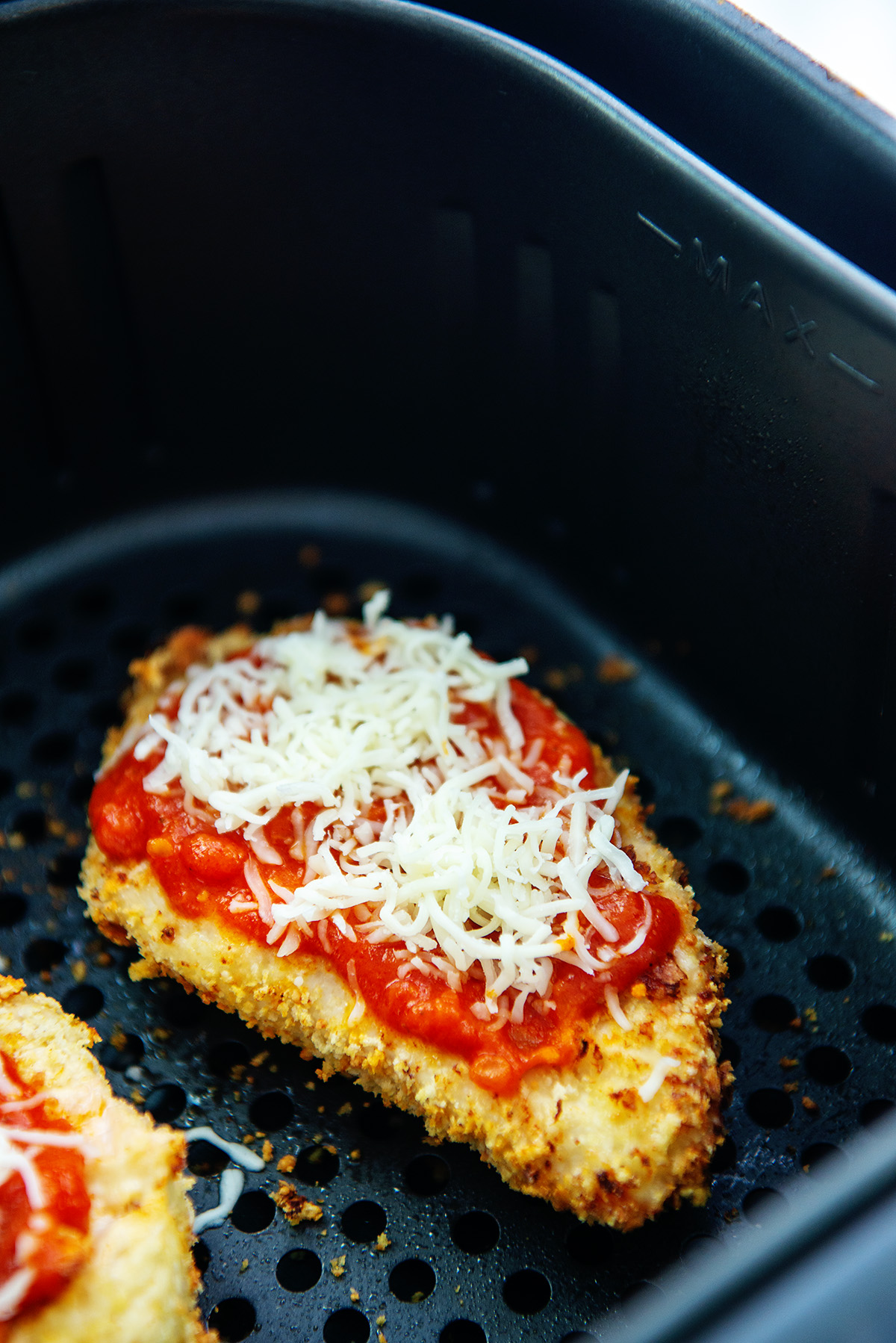 Cooked chicken parm with raw cheese on top in an air fryer basket