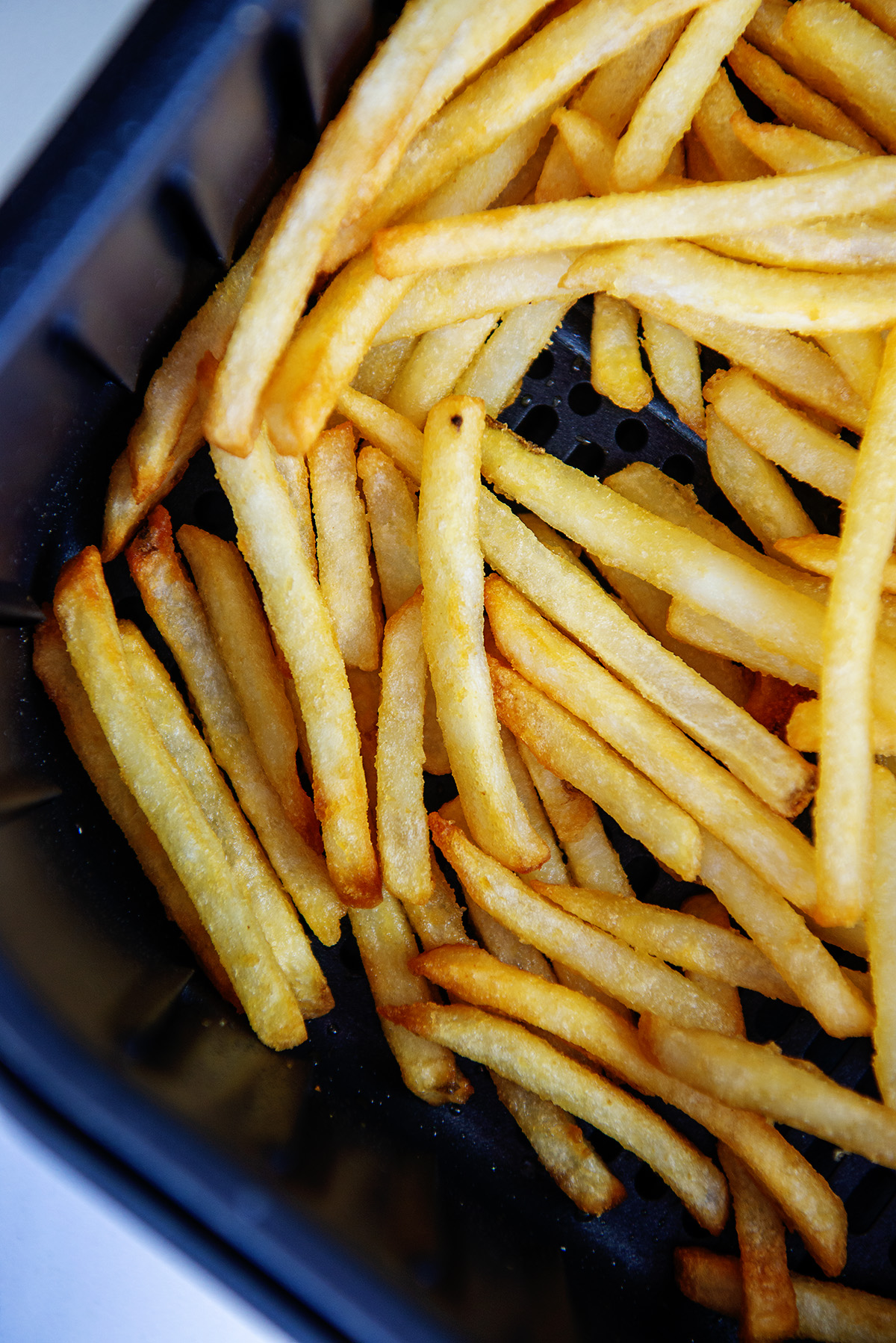 Closeup of cooked french fries stacked in an air fryer basket