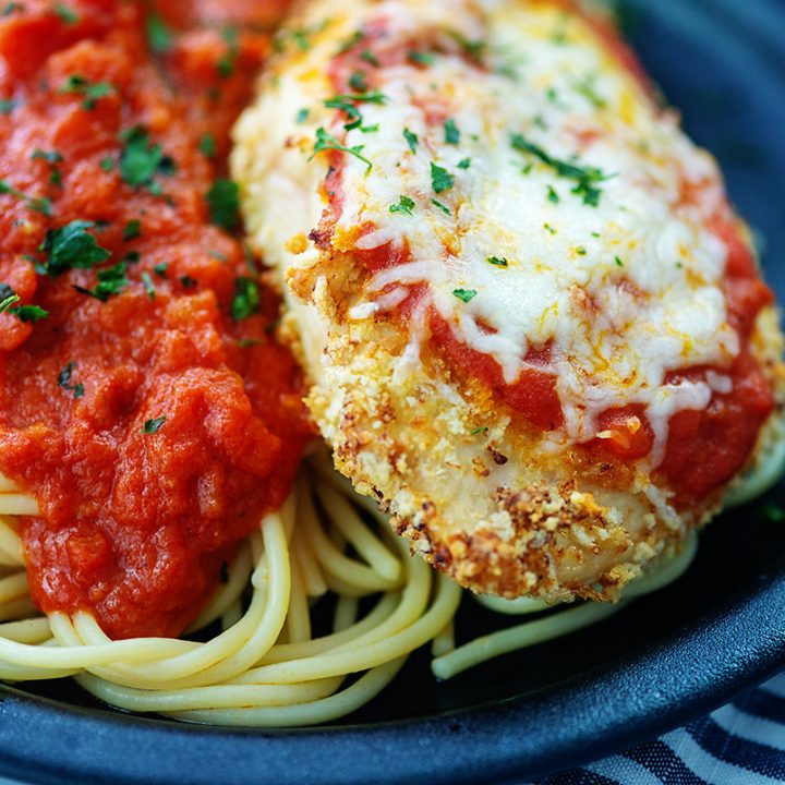 Close up of spaghetti and chicken parmesan on a black plate