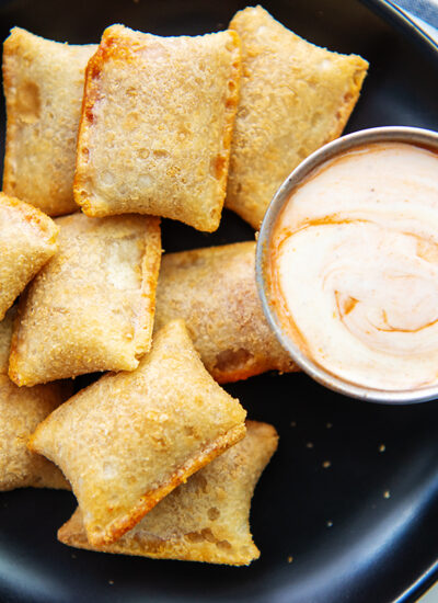 A close up of a black plate with pizza rolls and spicy ranch dressing on it.