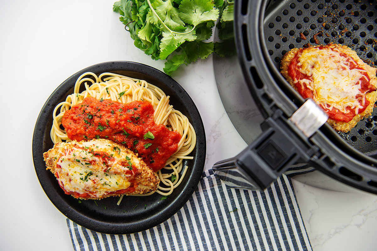 Overhead view of chicken parmesan next to an air fryer basket