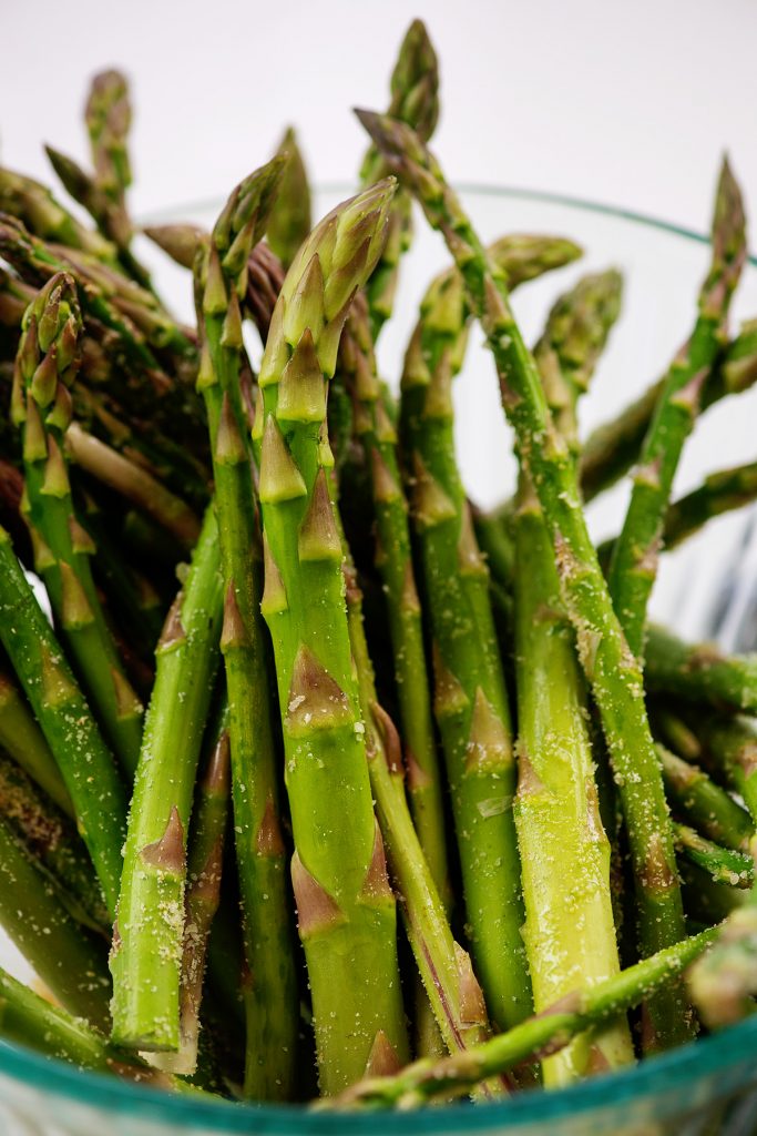 A closeup of seasoned asparagus in a glass bowl.