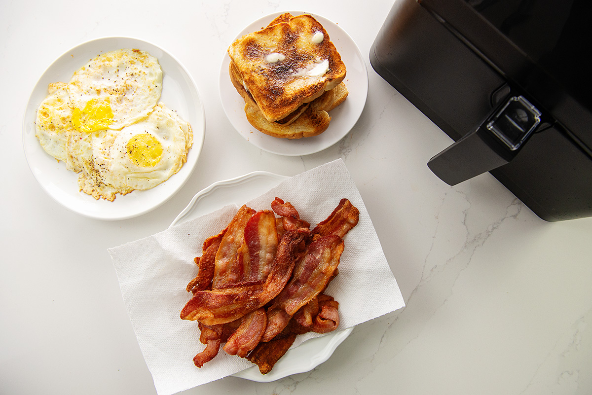 overhead view of bacon, eggs, and toast next to an air fryer.