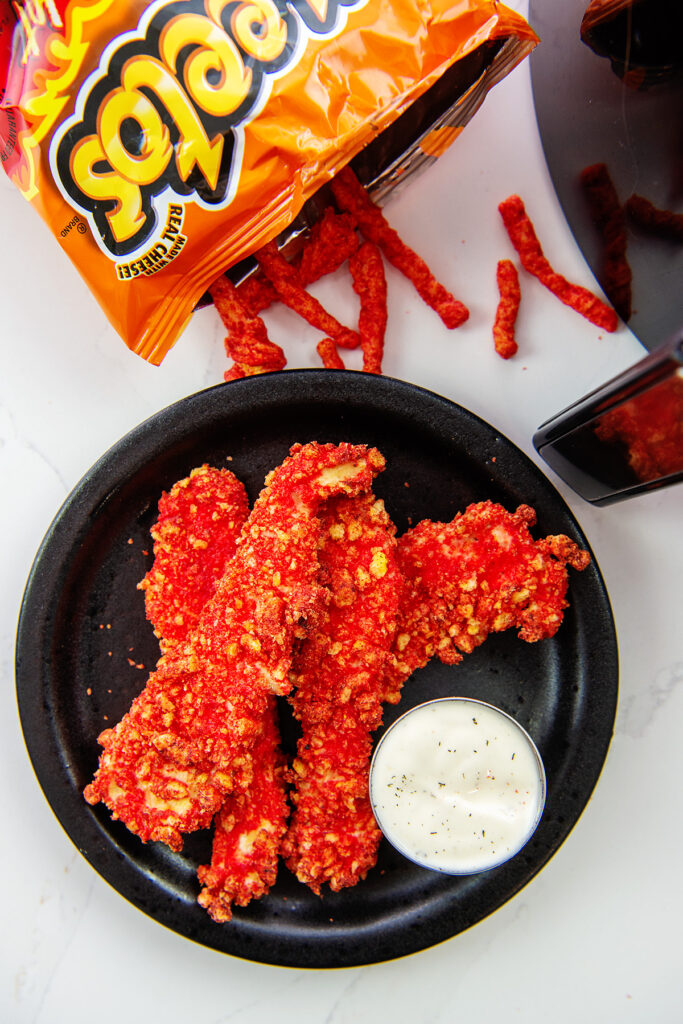 Overhead view of chicken strips and ranch dressing next to a bag of spilled cheetos