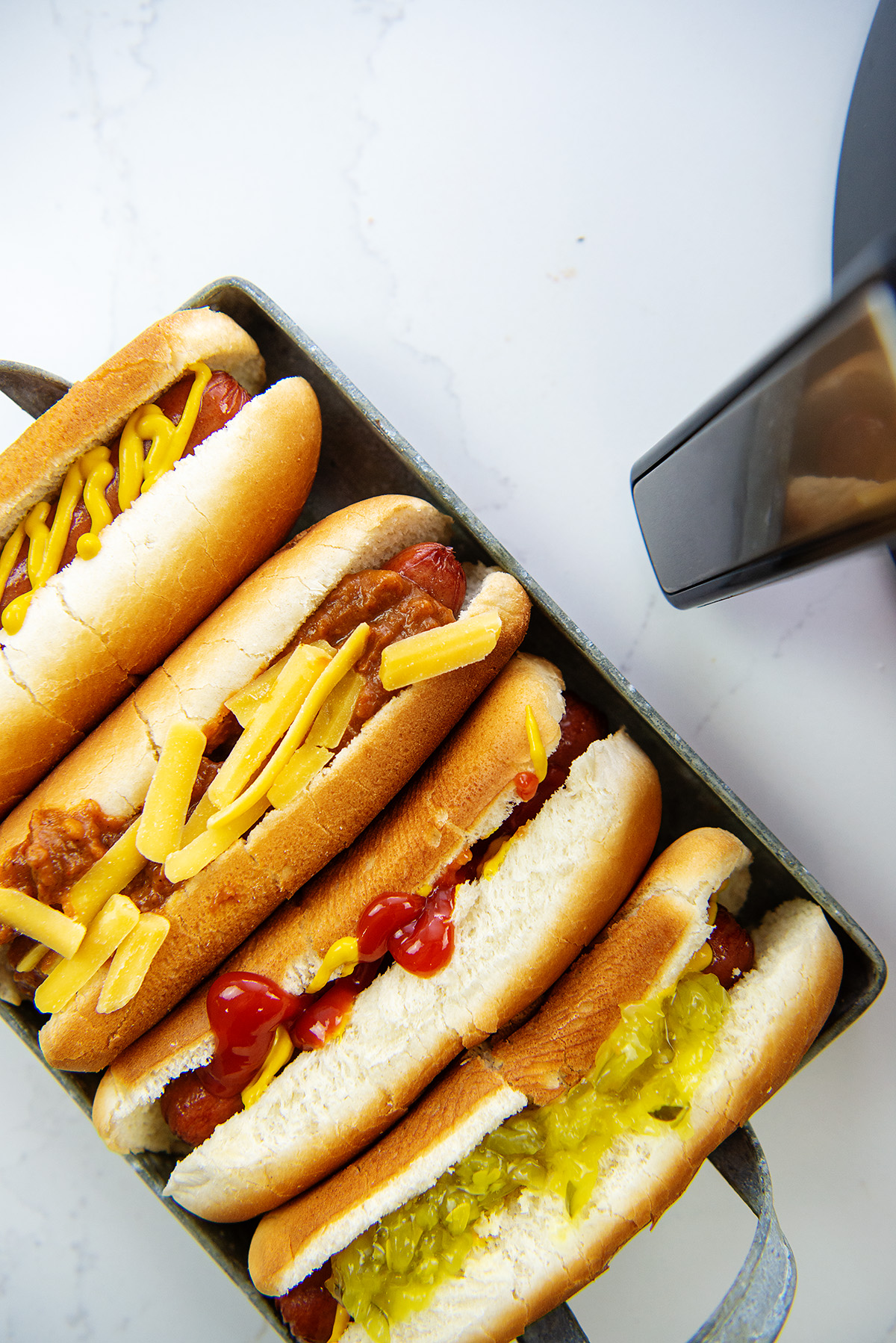 A close up of four hot dogs with various condiments on them in a serving tray
