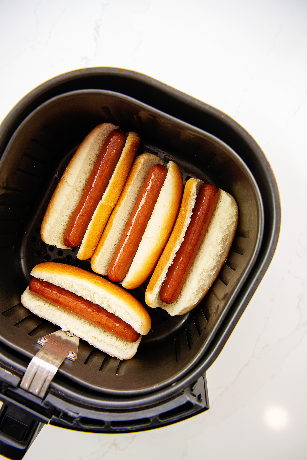 Overhead view of cooked hot dogs in an air fryer basket