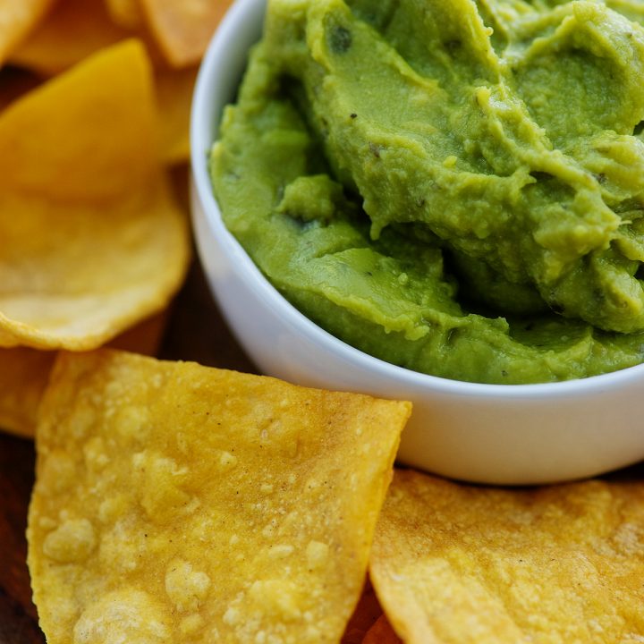 A cup of guacamole surrounded by tortilla chips