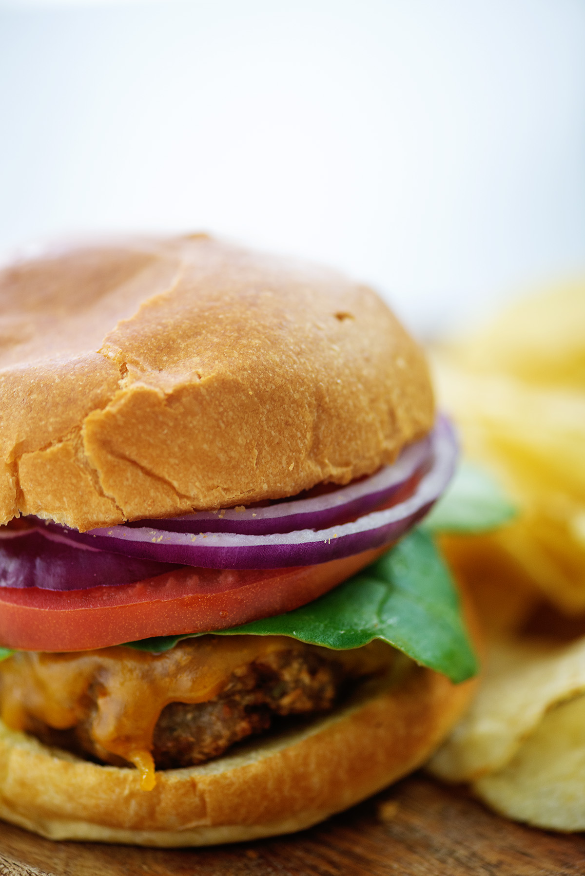 Close up of a turkey burger with onion, tomato, and lettuce on it next to a pile of chips