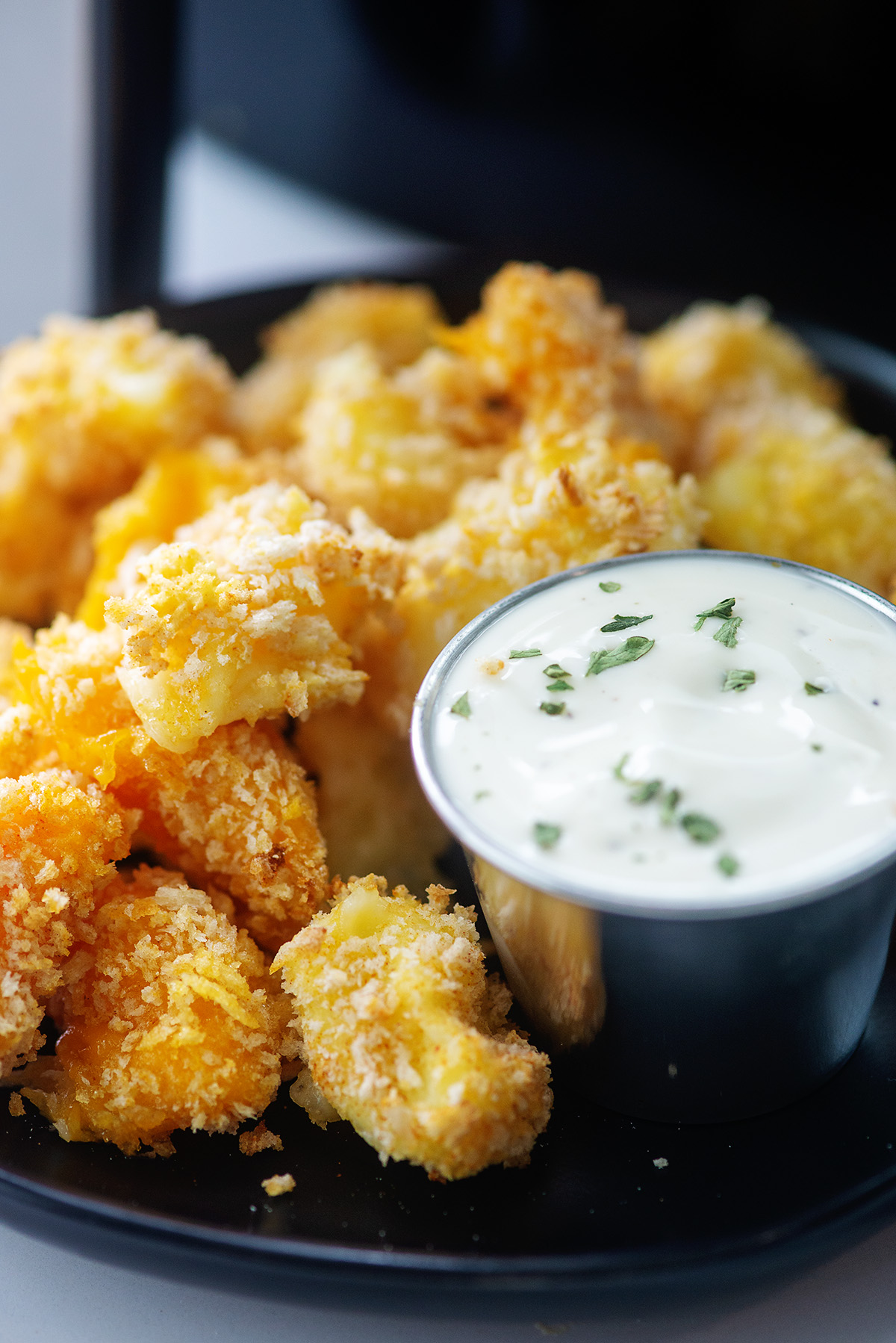 close up of cheese curds and ranch dressing on a black plate