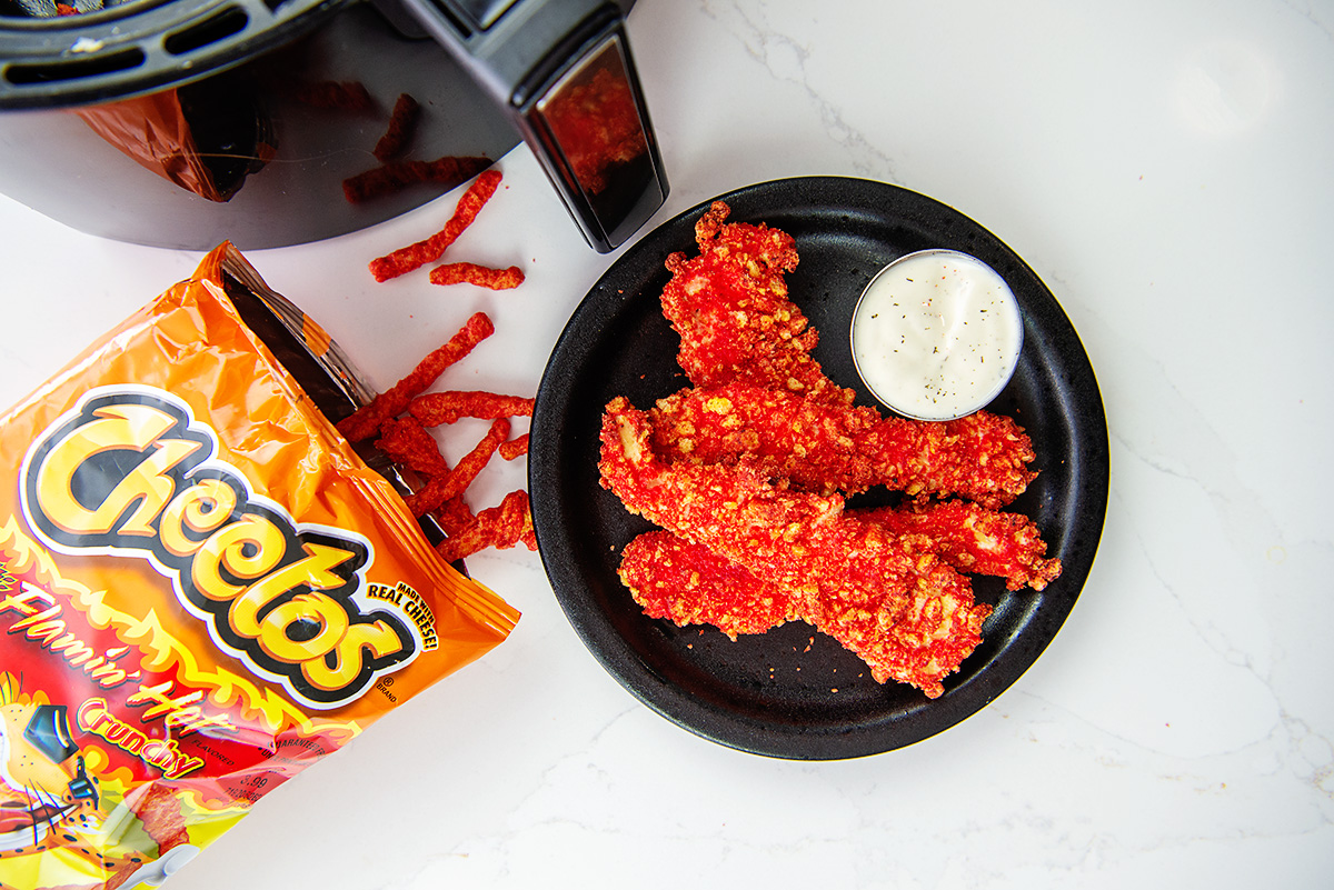 overhead view of cheetos spilling out of a bag next to a plate of chicken strips