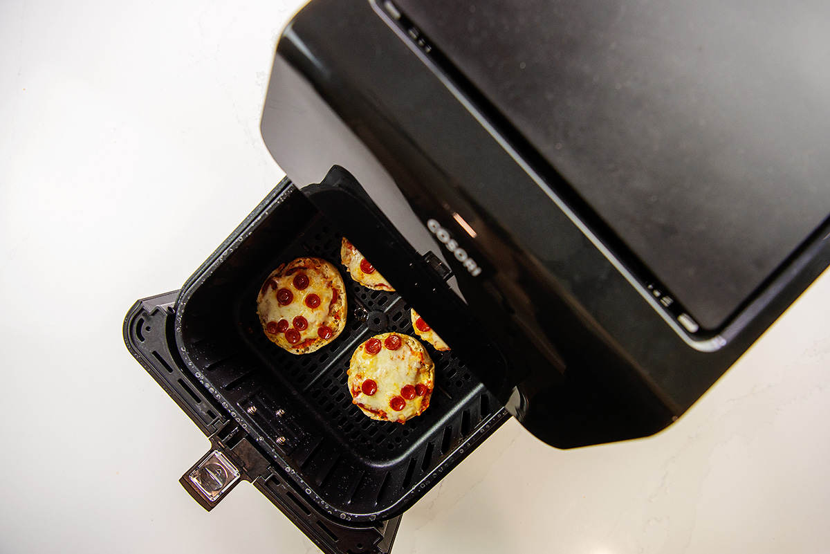 Overhead view of partially opened air fryer basket with cooked mini pizzas in it.