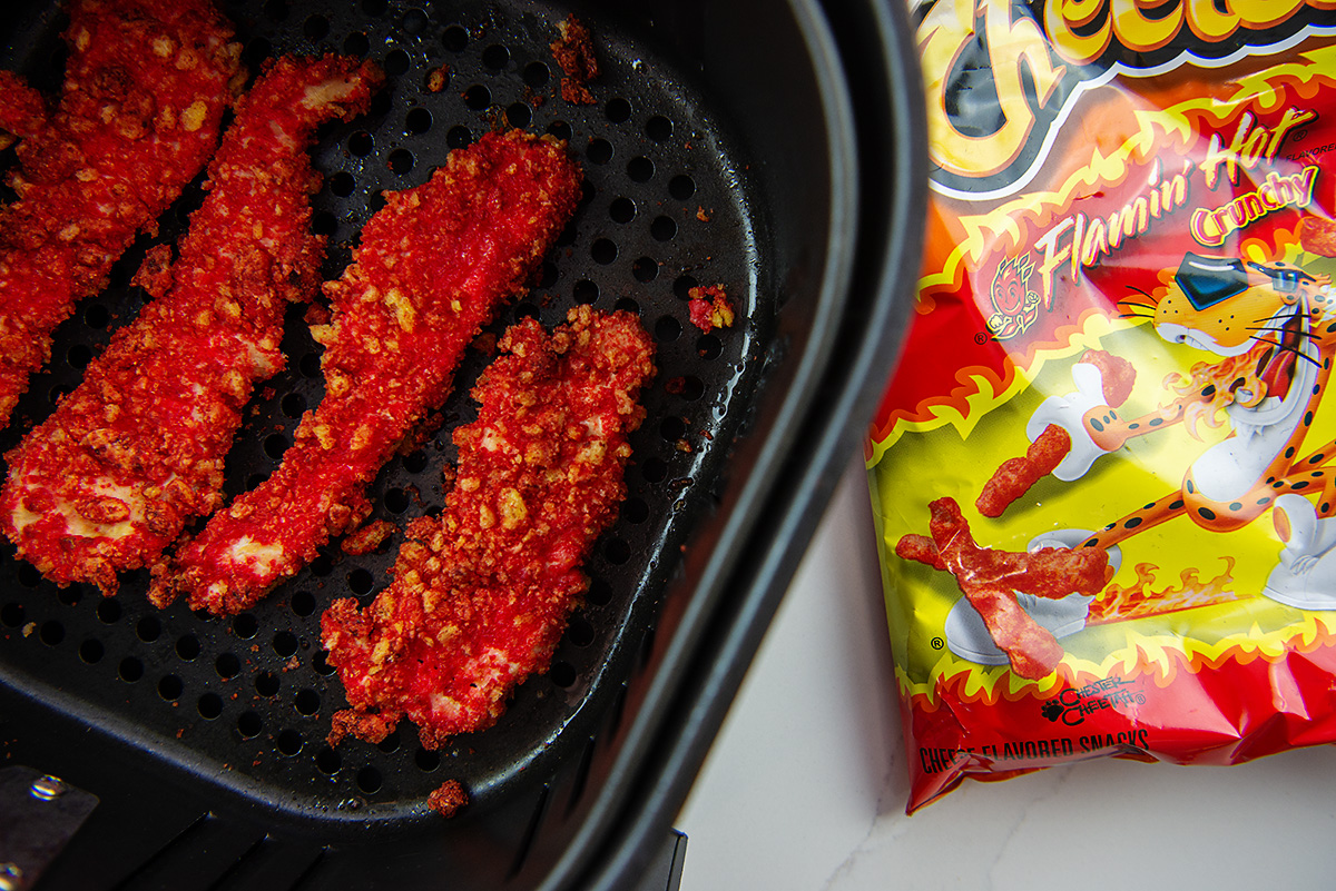 cheetos next to an air fryer basket with coated chicken strips in it.