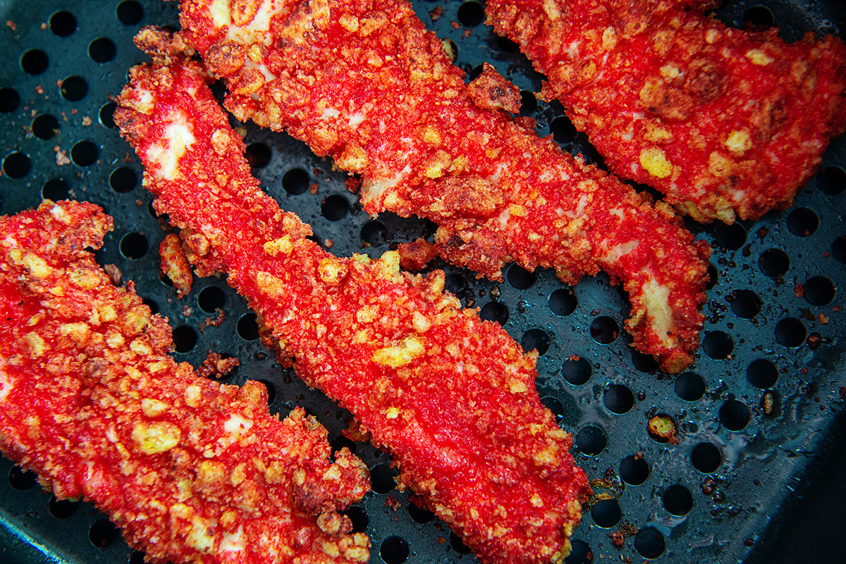 Close up of chicken strips coated in cheetos cooking in an air fryer basket