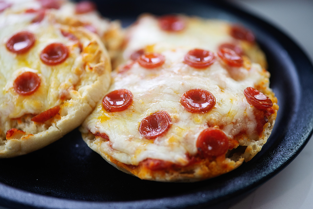 Two english muffin pizzas on a black plate