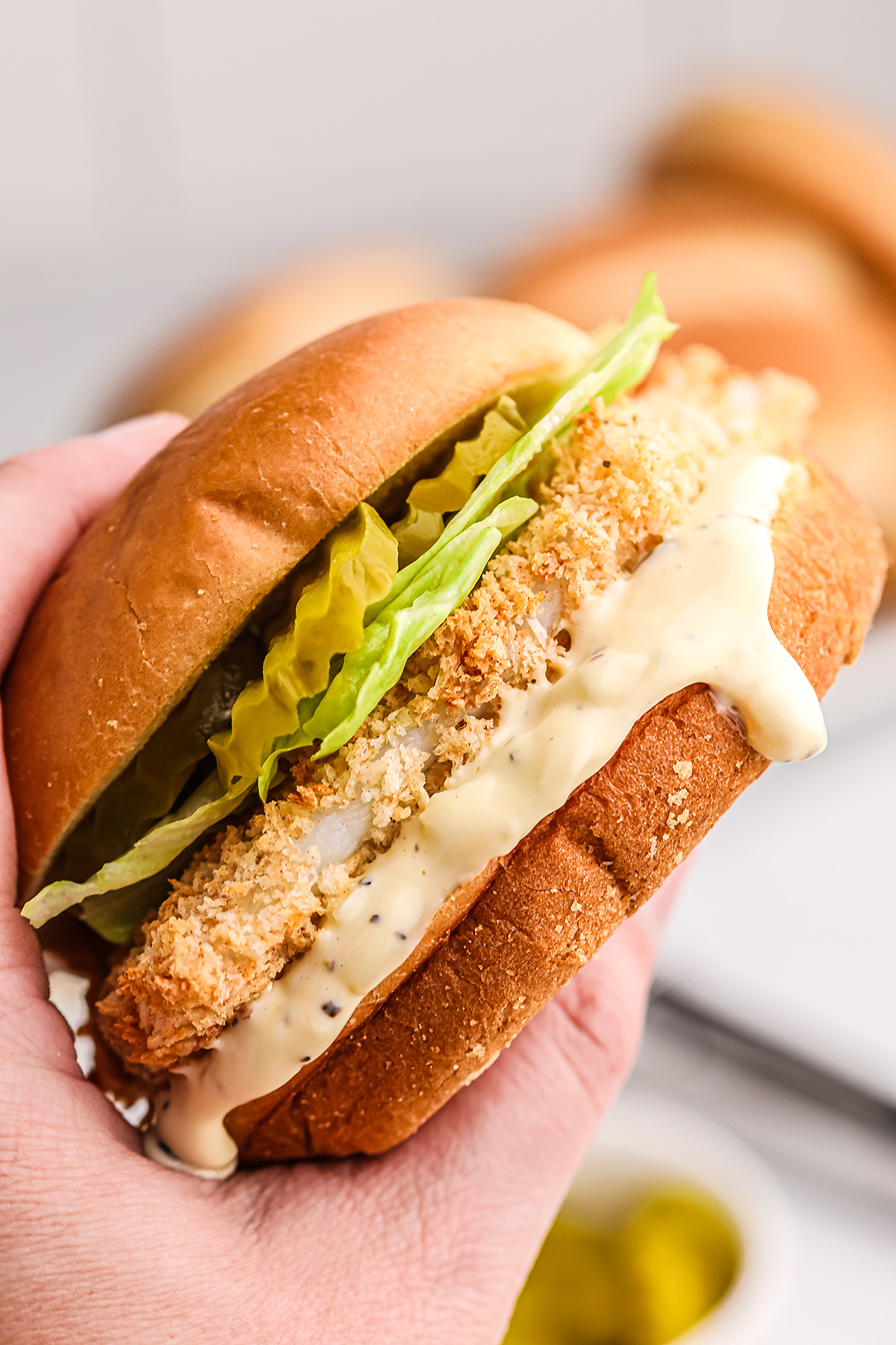 a person holding up a fish sandwich with tartar sauce