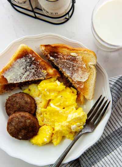 Close up of sausage patties on a white plate with scrambled eggs and toast