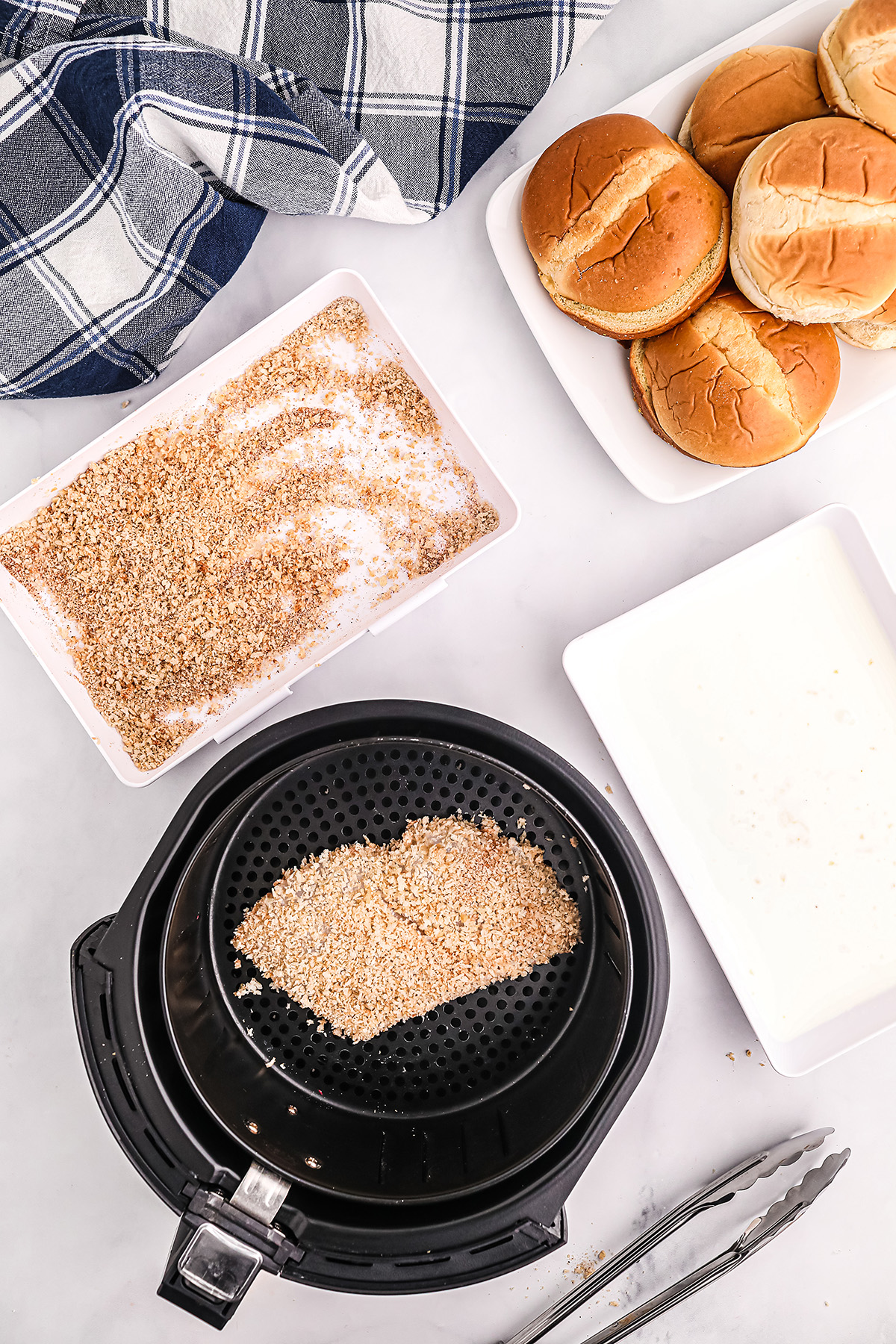 breaded fish filet in an air fryer basket next to buns