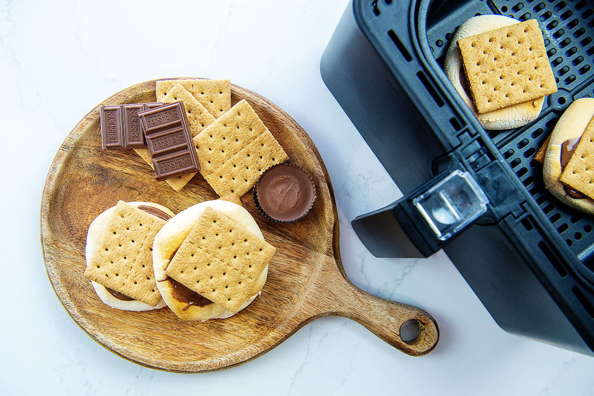 smores on a wooden plate next to an air fryer