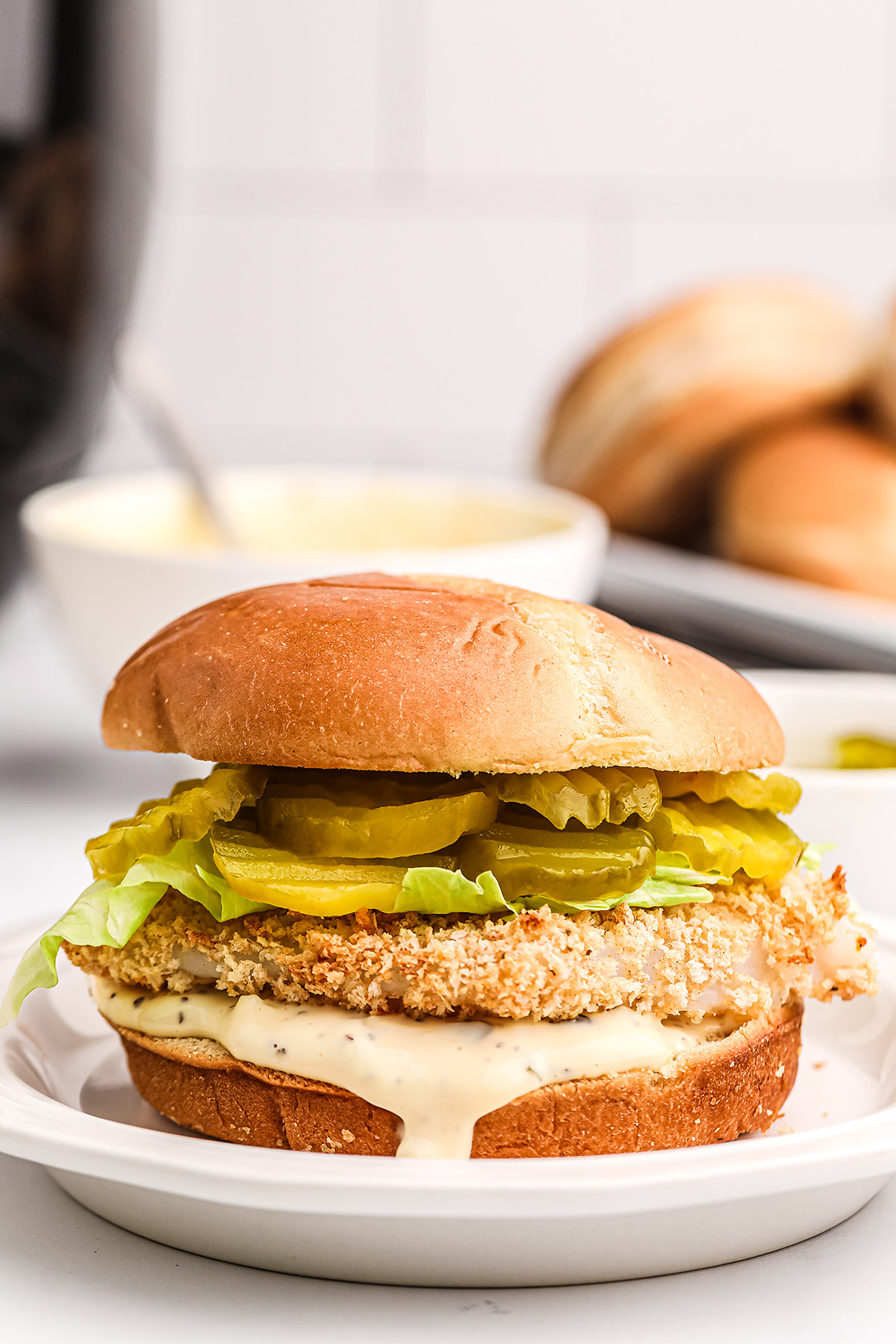 A close up of a fish sandwich in front of a bowl of tartar sauce