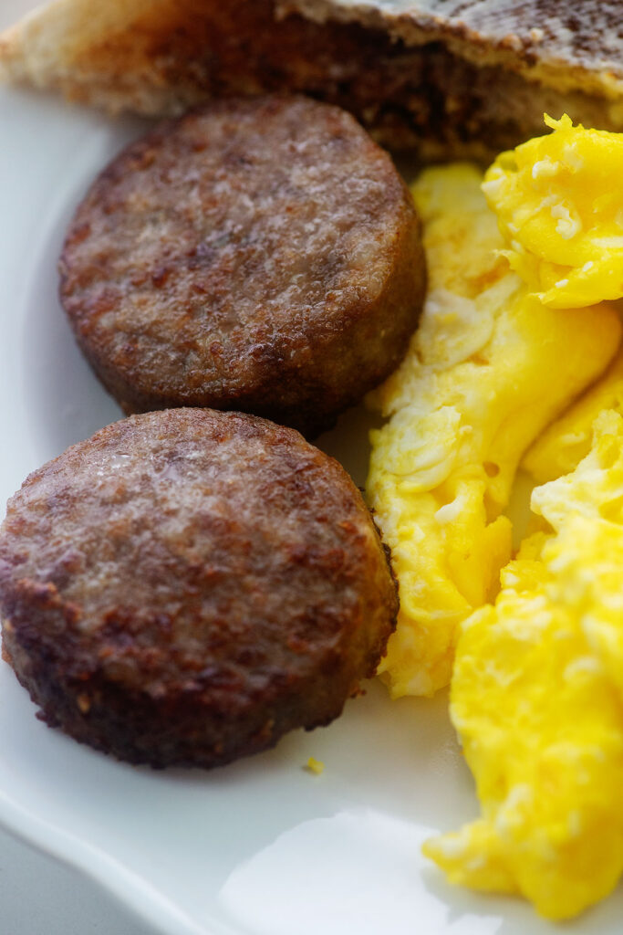 Close up of sausage patties on a white plate with scrambled eggs