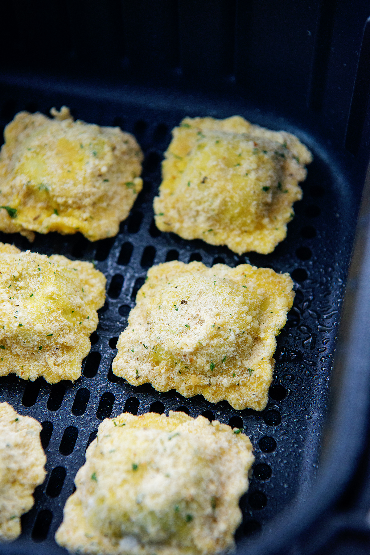 breaded ravioli in air fryer basket.