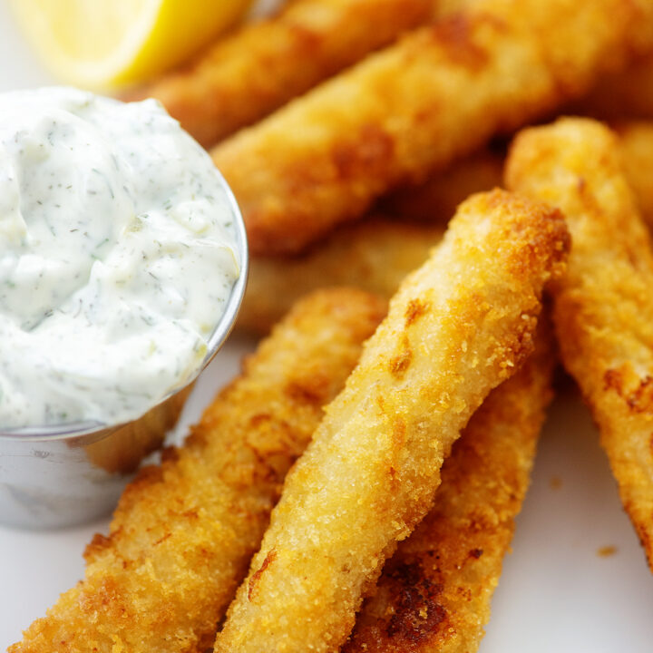 Fish sticks and tartar sauce on a white plate.