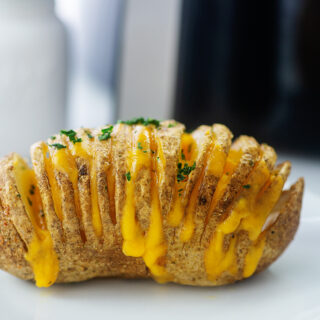 close up of a cheesy hasselback potato on a small white plate
