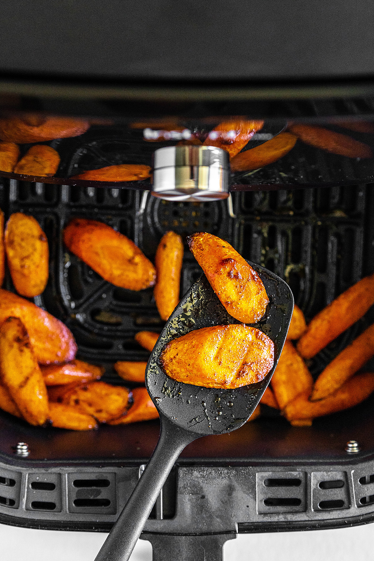 A large spoon with carrots on it above an air fryer basket