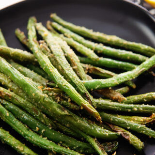 Close up of roasted green beans on a small black plate