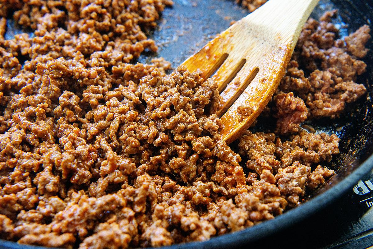 Ground beef being stirred in a skillet with a wooden spoon.