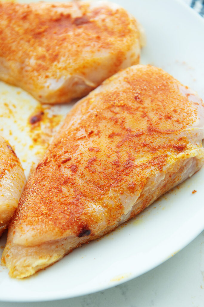 Seasoned raw chicken breasts on a white plate