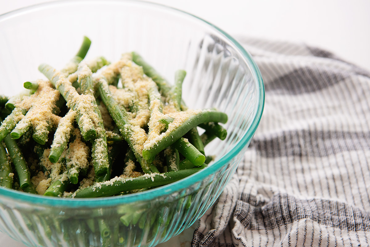 Close up of seasoning on top of raw green beans in a clear glass bowl