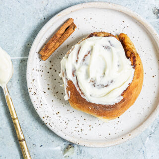 overhead view of a cinnamon roll on a plate next to a spoon of icing