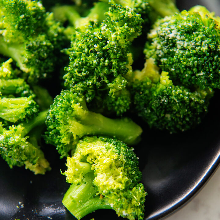 Close up of broccoli florets on a small black plate.