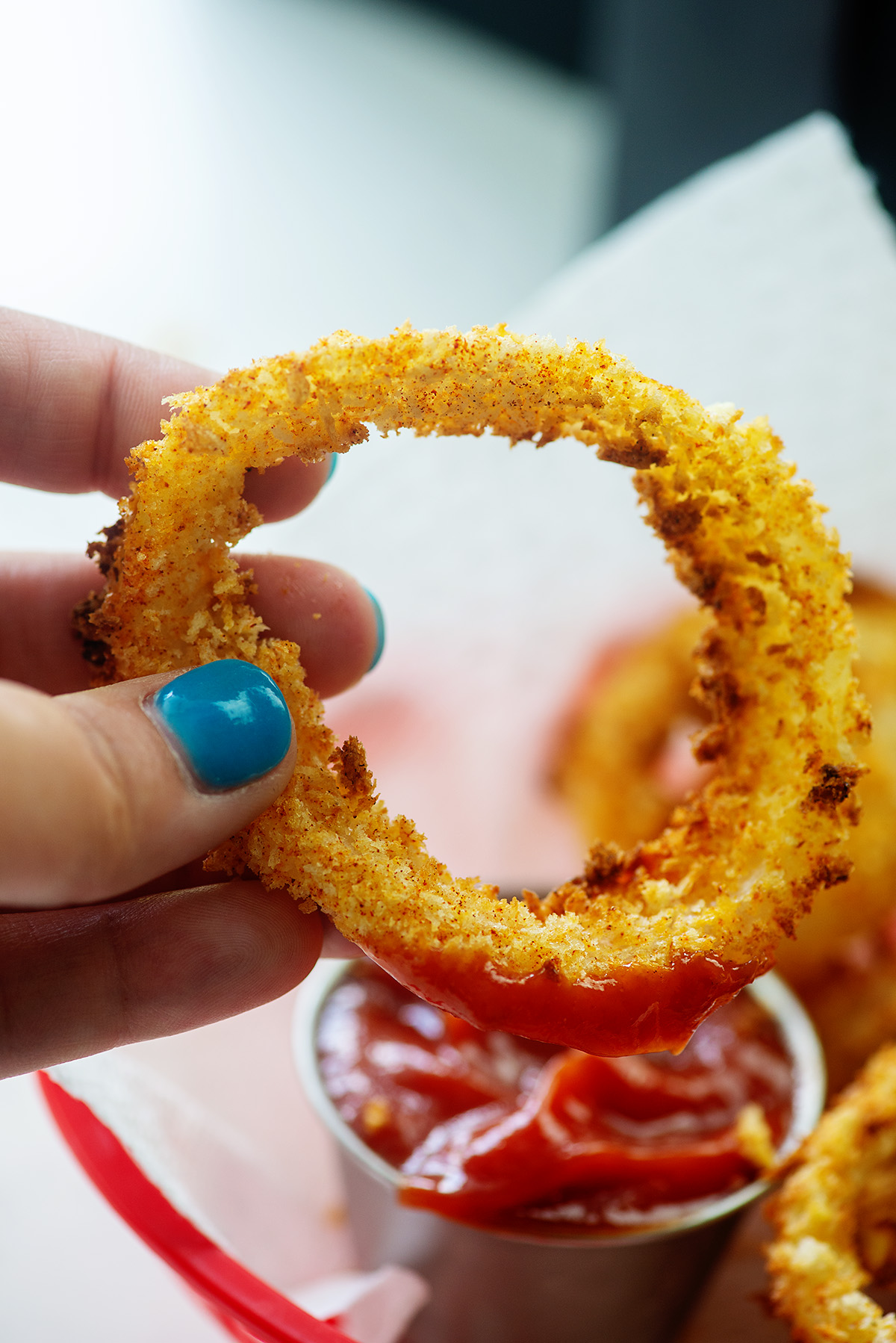 Close up of a woman holding an onion ring dipped in ketchup