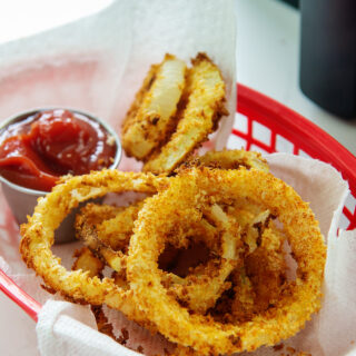 Onion rings in an appetizer basket with a cup of ketchup