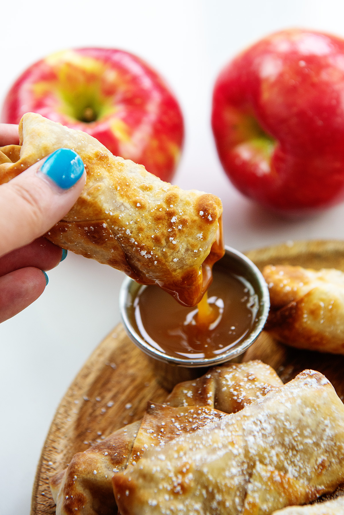 An apple pie egg roll being dipped into a cup of caramel