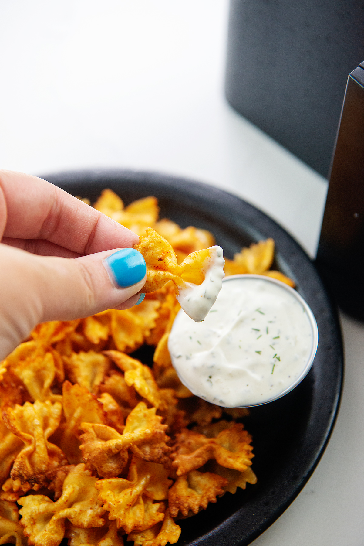 hand dipping a pasta chip into ranch dressing.