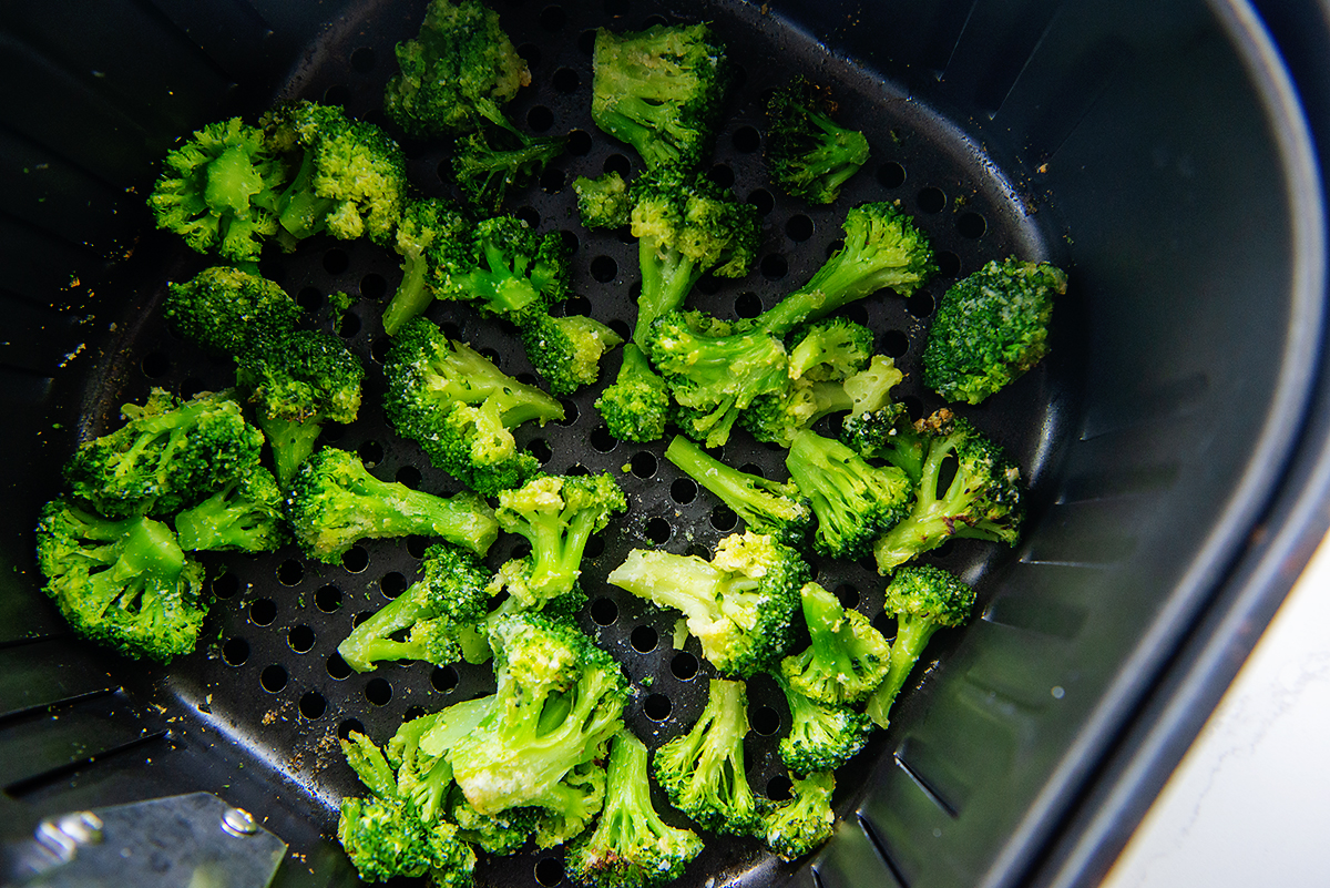 Close up of seasoned broccoli in an air fryer basket