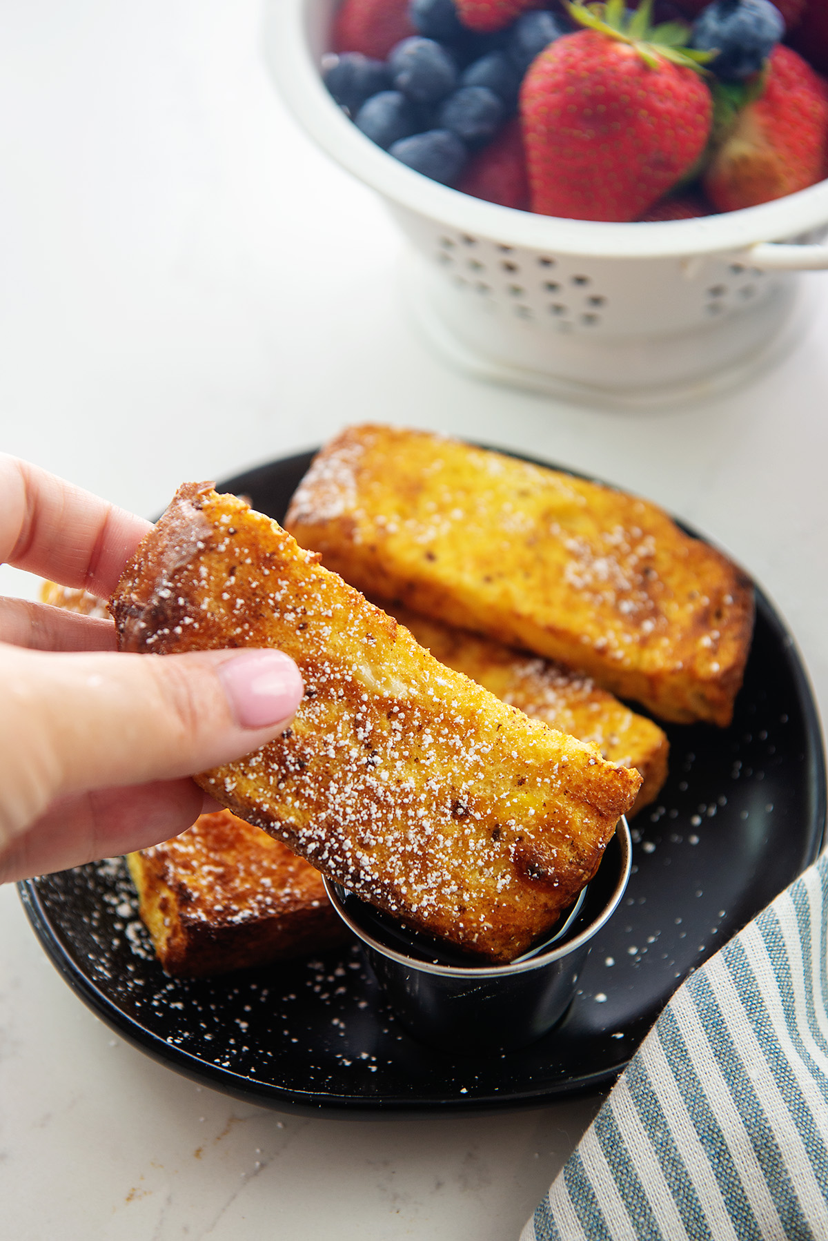 A woman dipping a French toast stick into a cup of syrup