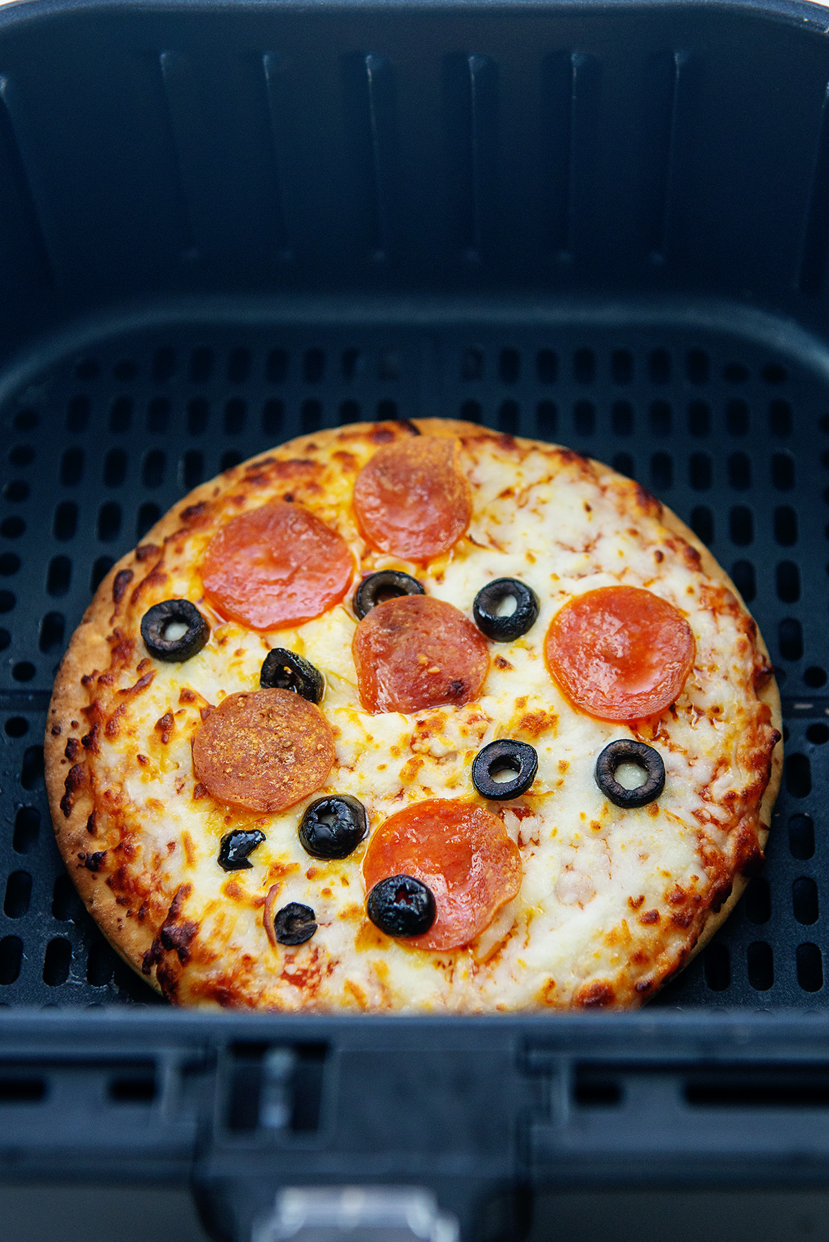 A cooked pepperoni and olive pizza in an air fryer basket.