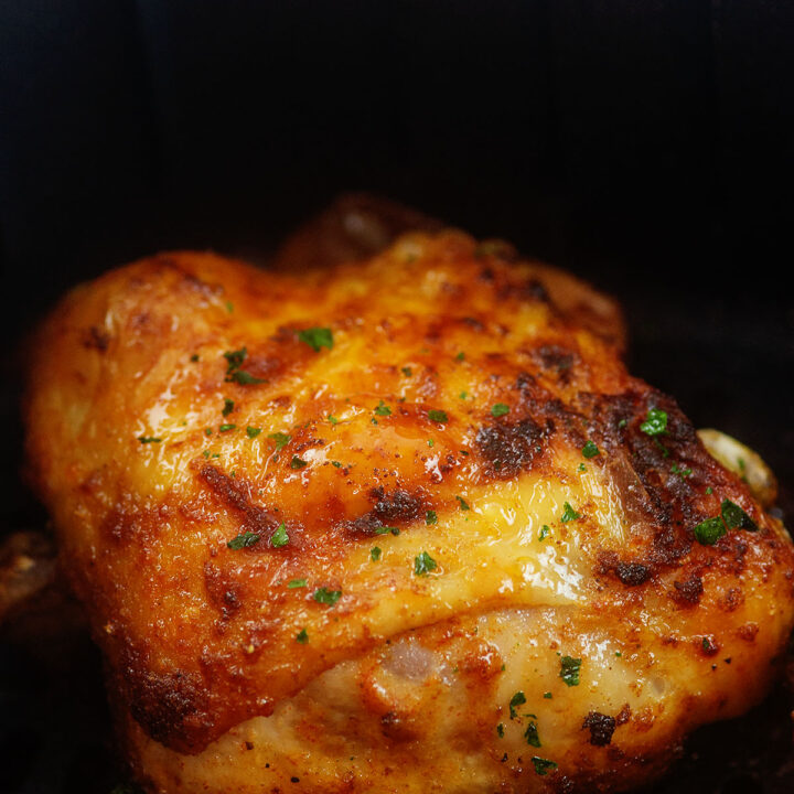 close up of cooked and seasoned chicken thigh in an air fryer basket.
