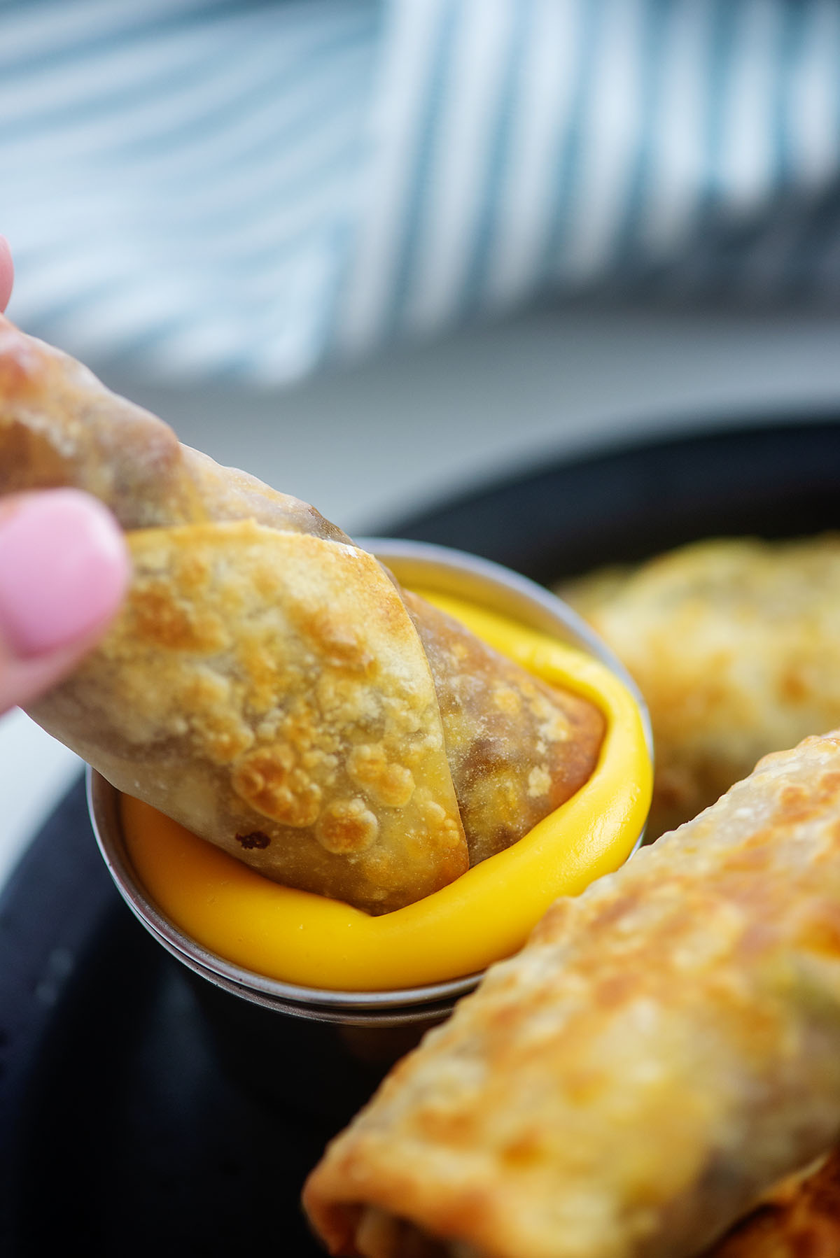 A cheesesteak egg roll being dipped into cheese