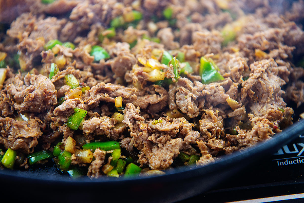 Shaved steak, onions and peppers cooking in a skillet