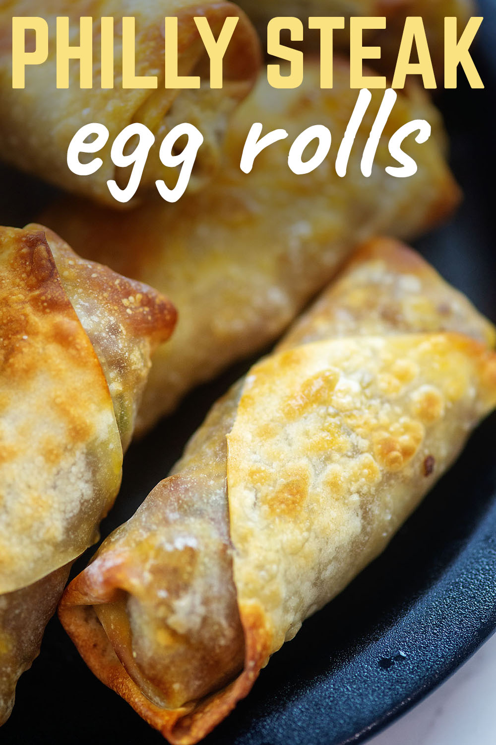 Close up of egg rolls on a black plate.